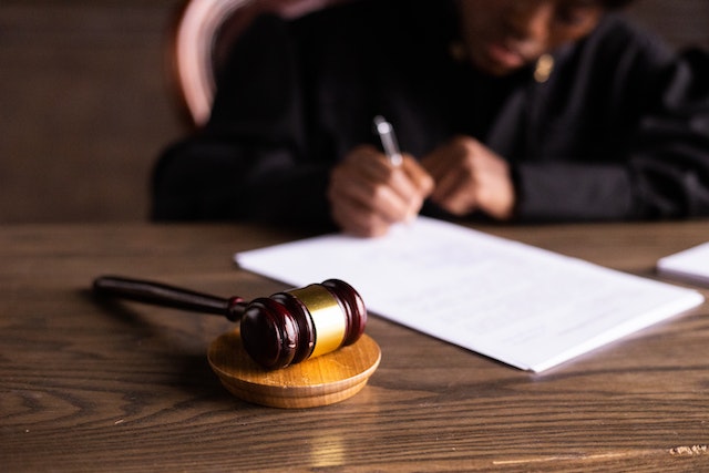 A gavel sits on a desk while a judge signs a legal document in their department